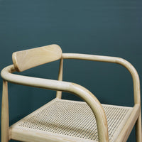 Natural wood color chair with a woven cane seat against a deep green background, showcasing minimalist design.