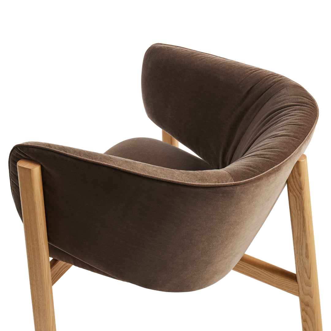 Brown velvet upholstered chair with natural wooden legs, featuring a smooth, curved design. Perfect for modern decor.