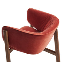 Rust-colored velvet armchair with smooth texture and curved design, featuring wooden legs. Stylish and modern accent piece.