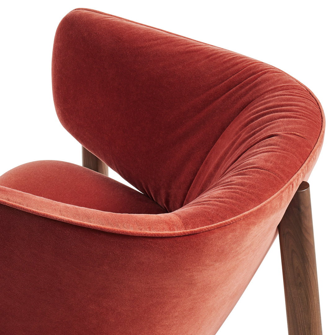 Soft velvet armchair in warm terracotta with smooth curves and a subtle sheen, complemented by wooden legs.