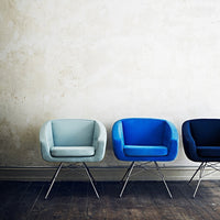 Three modern chairs in soft blue, vibrant cobalt, and deep navy against a textured wall, highlighting minimalist design.