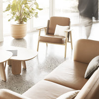 Light tan armchair and sofa with a patterned cushion, set against a bright, modern interior and speckled floor.