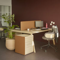 Modern office desk in light wood with brown accents, complemented by green foliage and a burgundy wall background.