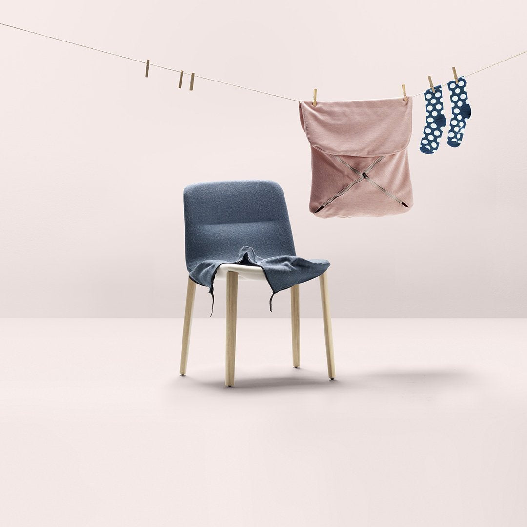 Blue upholstered chair with a light pink and polka dot cloth hanging nearby, set against a minimalistic background.