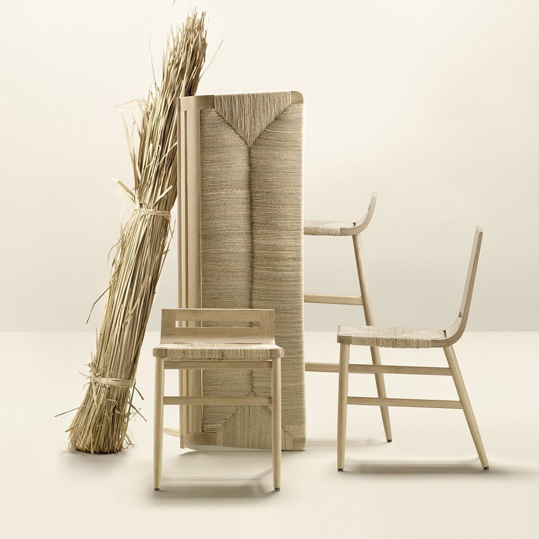 Natural beige chairs with woven seats displayed alongside a textured straw bundle and backdrop, creating a minimalist aesthetic.