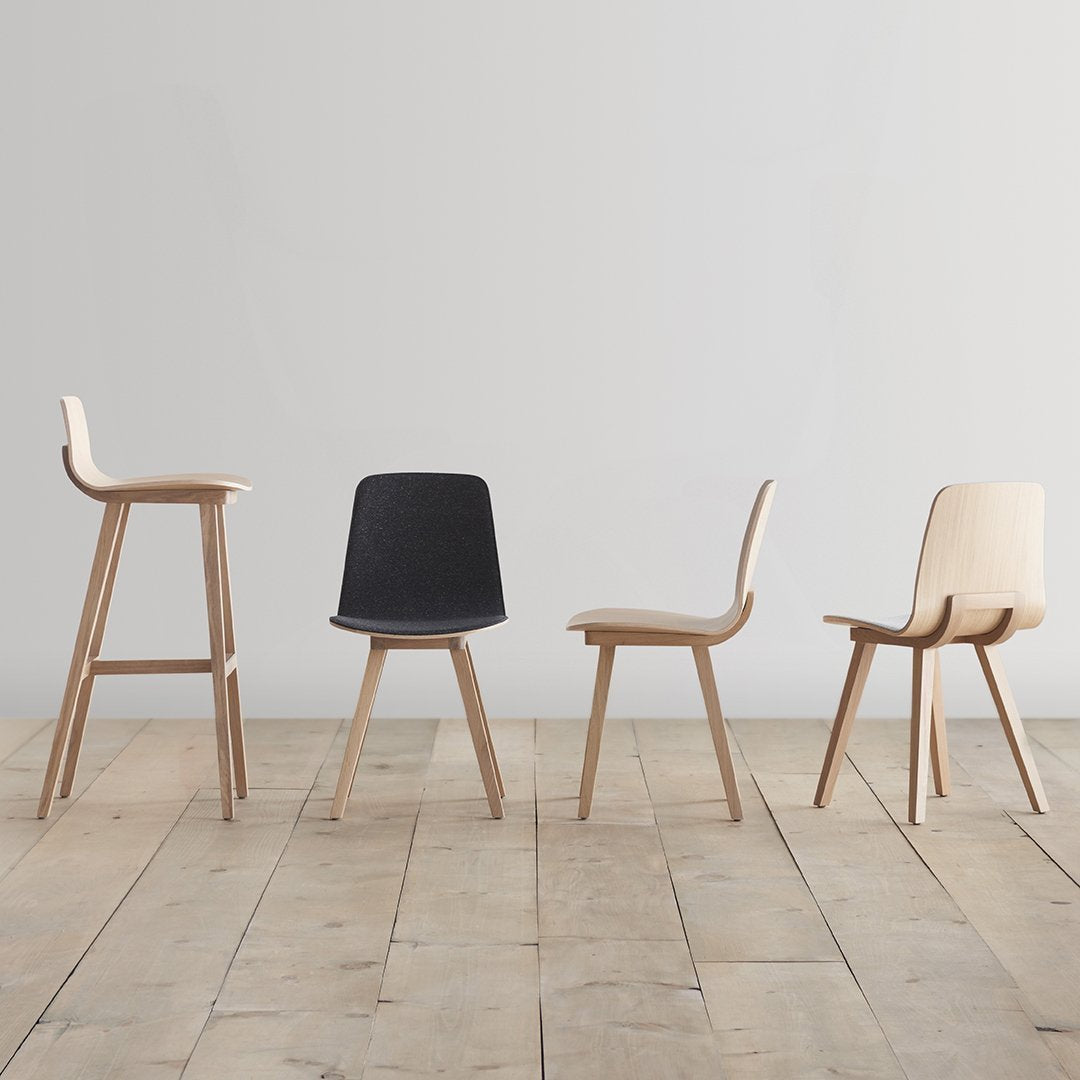 Set of four minimalist chairs featuring natural wood tones, sleek black, and soft cream finishes on a wooden floor.