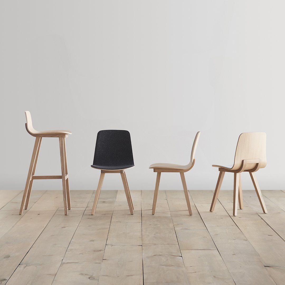 Set of four modern wooden chairs in light wood, featuring black and natural finishes, on a rustic wooden floor.