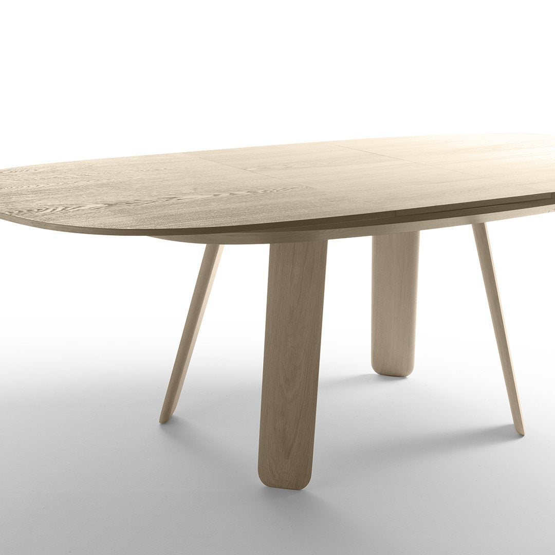 Light wood oval dining table with smooth surface and minimalist design, showcasing natural grain patterns and neutral tones.