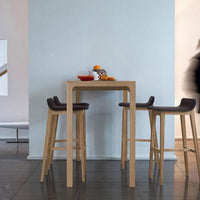 Wooden bar table with natural finish and sleek design, paired with dark brown upholstered stools against a light blue wall.