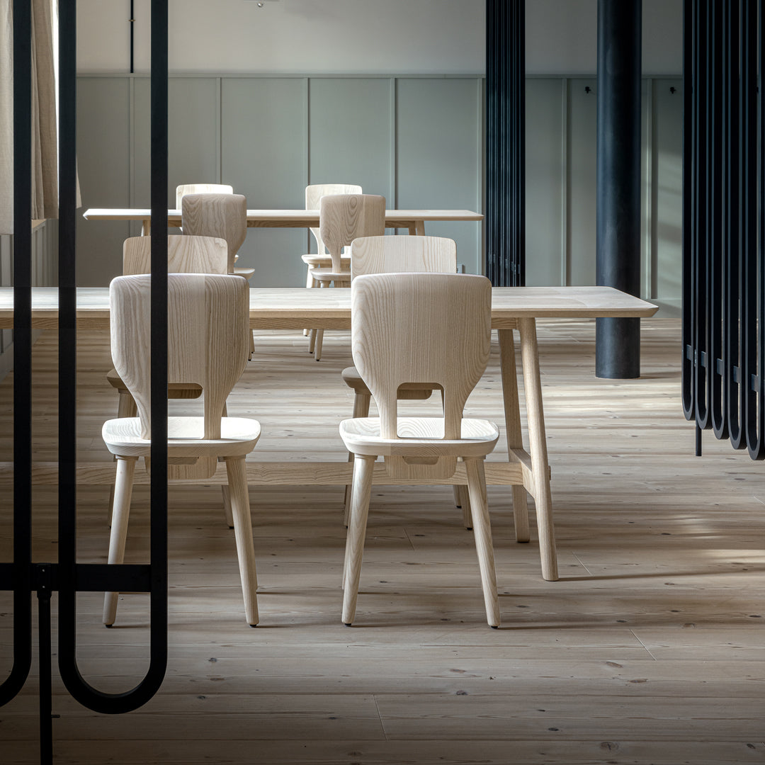 Light wooden dining table and chairs with a natural finish, set in a contemporary, minimalist interior.
