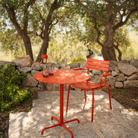 Vibrant red metal table and chair set amidst natural greenery and stone, perfect for outdoor dining.