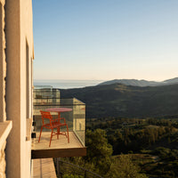 "Vibrant red chair on a glass balcony, overlooking lush green hills and a clear blue sky."