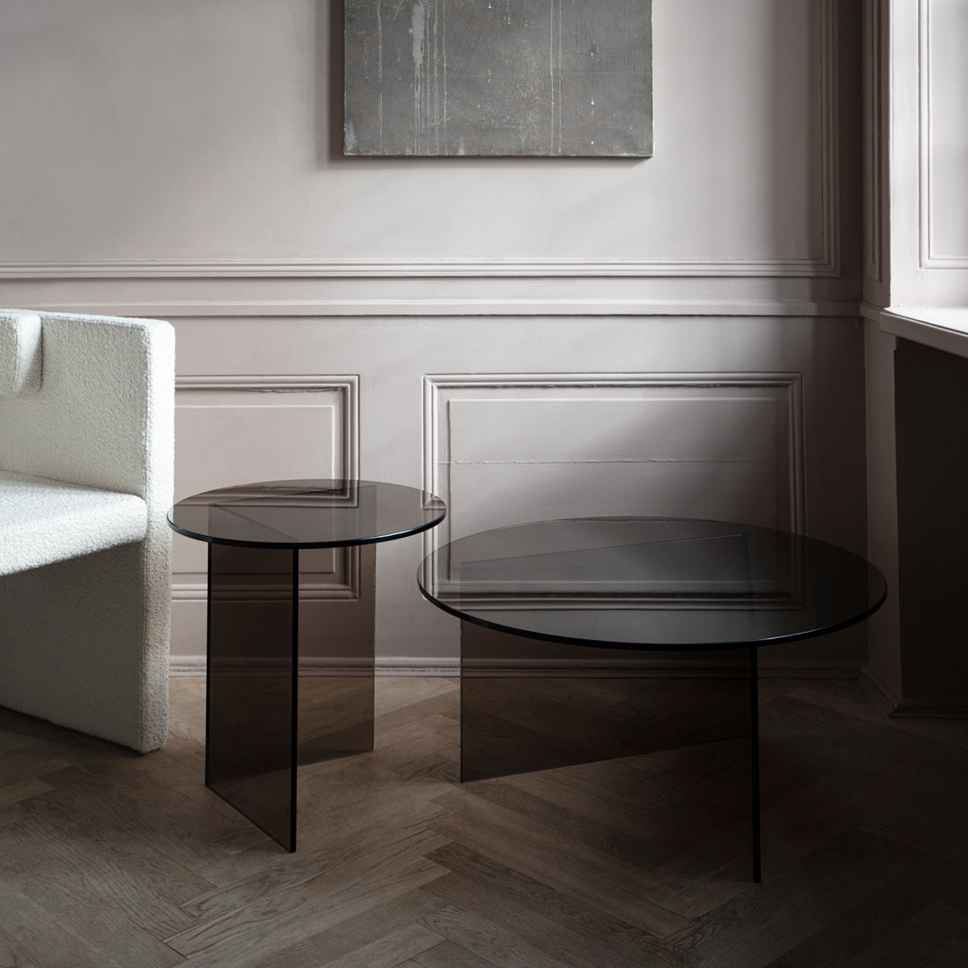 Black round glass coffee tables with sleek designs, set against a light-colored wall and wooden floor.