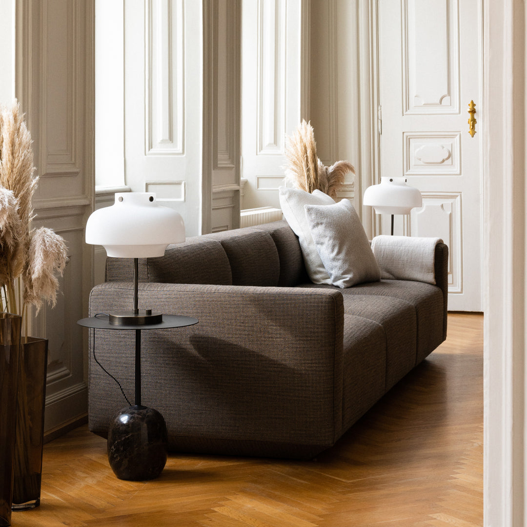Brown textured sofa with light gray cushions, paired with a sleek black lamp and warm wooden flooring.