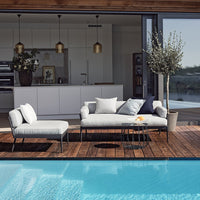 Stylish outdoor seating with light gray cushions, dark frame, and a chic blue accent pillow by the serene poolside.