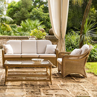 Light beige cushions on a wicker seating set with natural tones, contrasting with lush green outdoor surroundings.