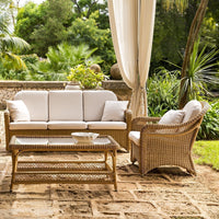 Cream-colored cushions on a stylish wicker sofa set with natural tones, surrounded by lush greenery.