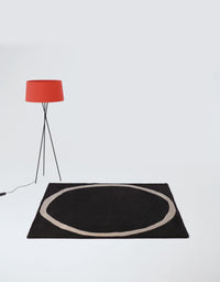 Black rug with circular beige pattern, complemented by a stylish orange lamp for a modern aesthetic.