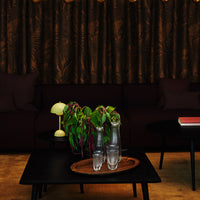 Dark brown patterned curtains with a rich texture, complemented by a black sofa and earthy wooden tones.