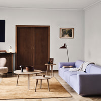 Light lavender sofa, beige accent chairs, round wooden tables, and a tan area rug in a modern living space.