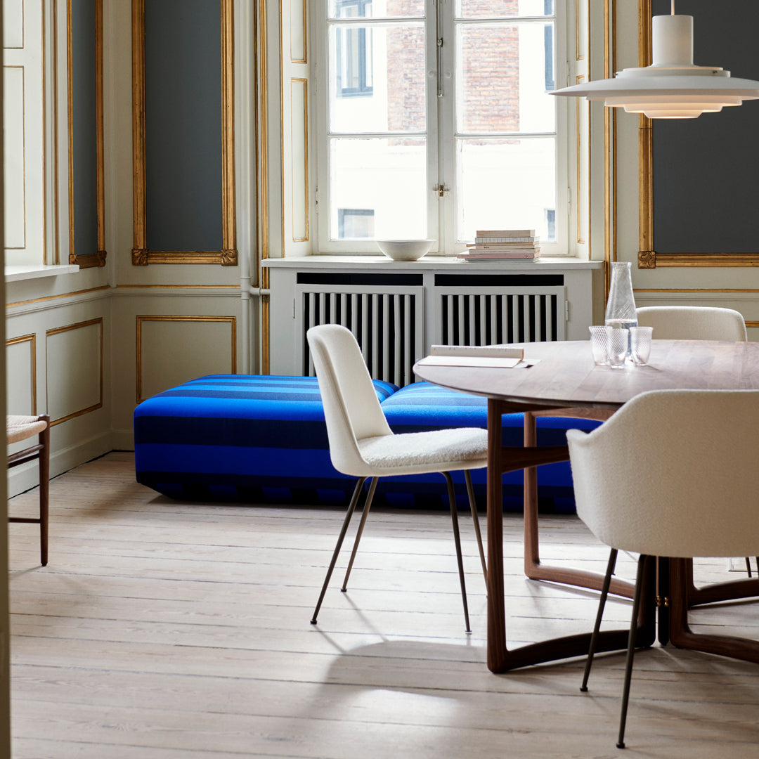 Blue striped ottoman in a stylish dining room with white chairs and elegant wooden accents.