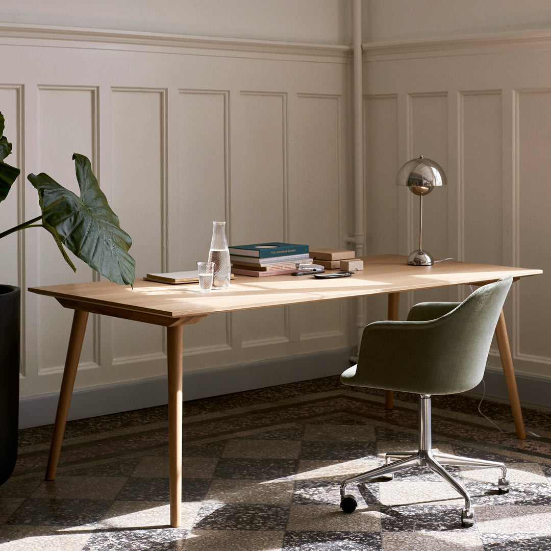 "Light wood desk with modern design, olive green chair, and neutral patterned floor tiles in bright, airy room."