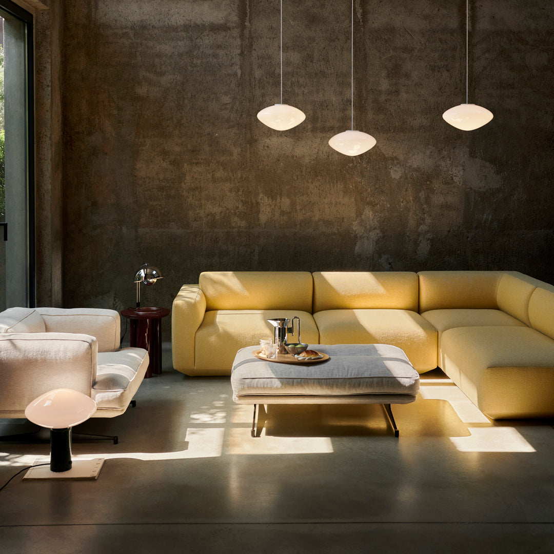 Modern living room featuring a yellow sectional sofa, white armchair, and minimalist decor against a concrete backdrop.