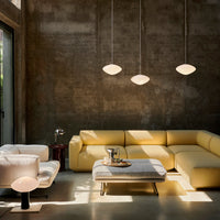 Modern living room featuring a yellow sectional sofa, minimalist white pendant lights, and a textured gray wall.