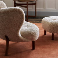 "Beige textured chair and ottoman on a warm terracotta rug, featuring soft, rounded shapes."
