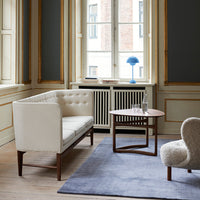 Elegant white tufted sofa, dark wood legs, round wooden table, cozy gray rug, and soft beige accent chair in a modern interior.