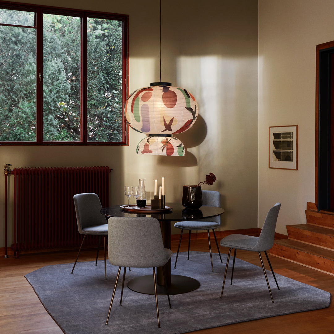 Colorful patterned lamp hanging above a modern dining table with gray chairs on a round rug in a warm, inviting room.