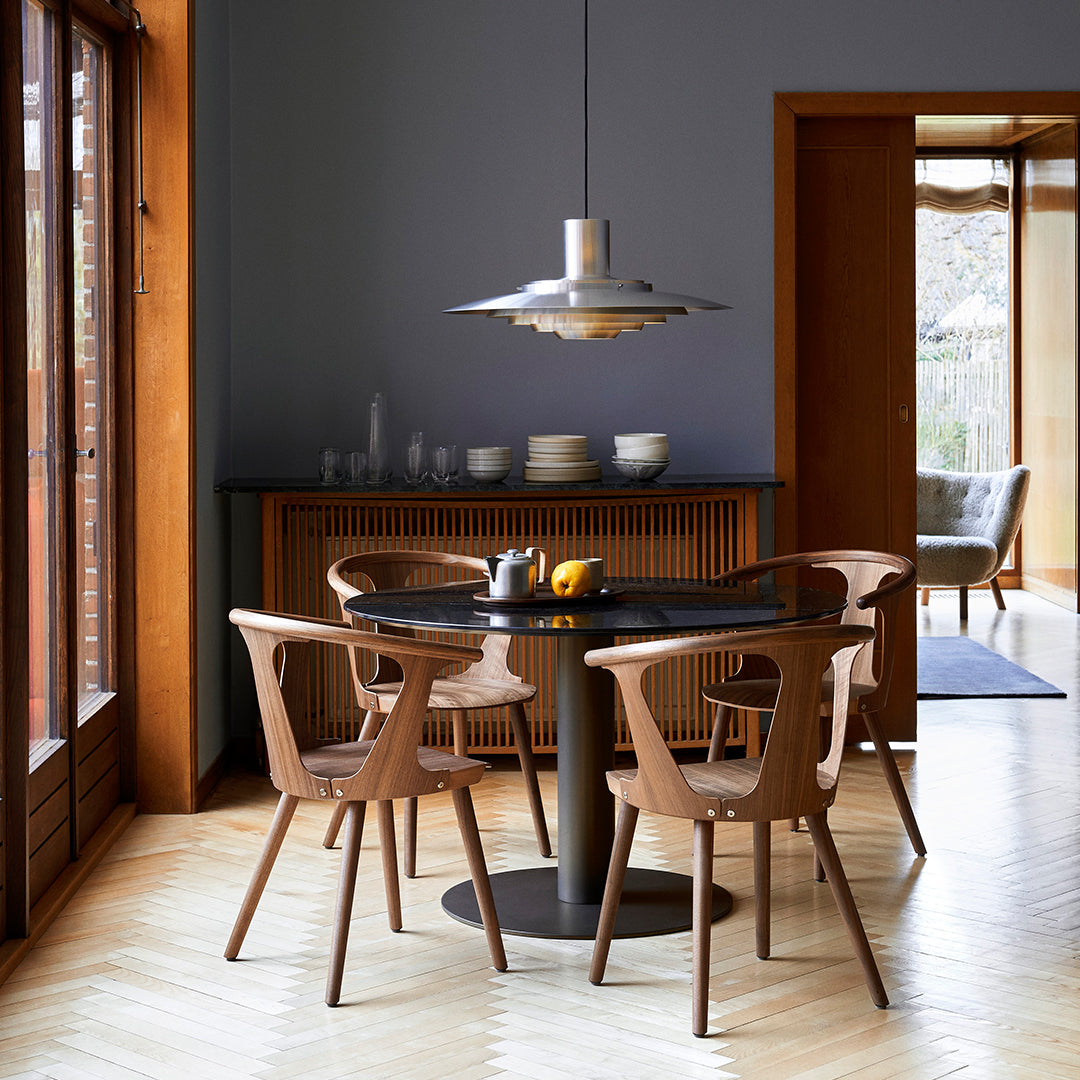 Elegant wooden dining chairs surround a sleek black round table, set against warm wood tones and soft gray walls.