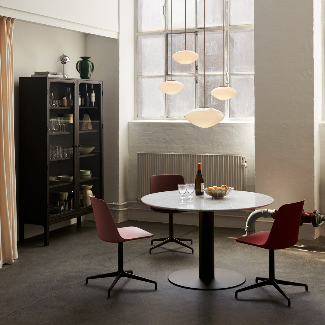 Modern dining set featuring a white round table, red chairs, and warm hanging light fixtures in a stylish interior.
