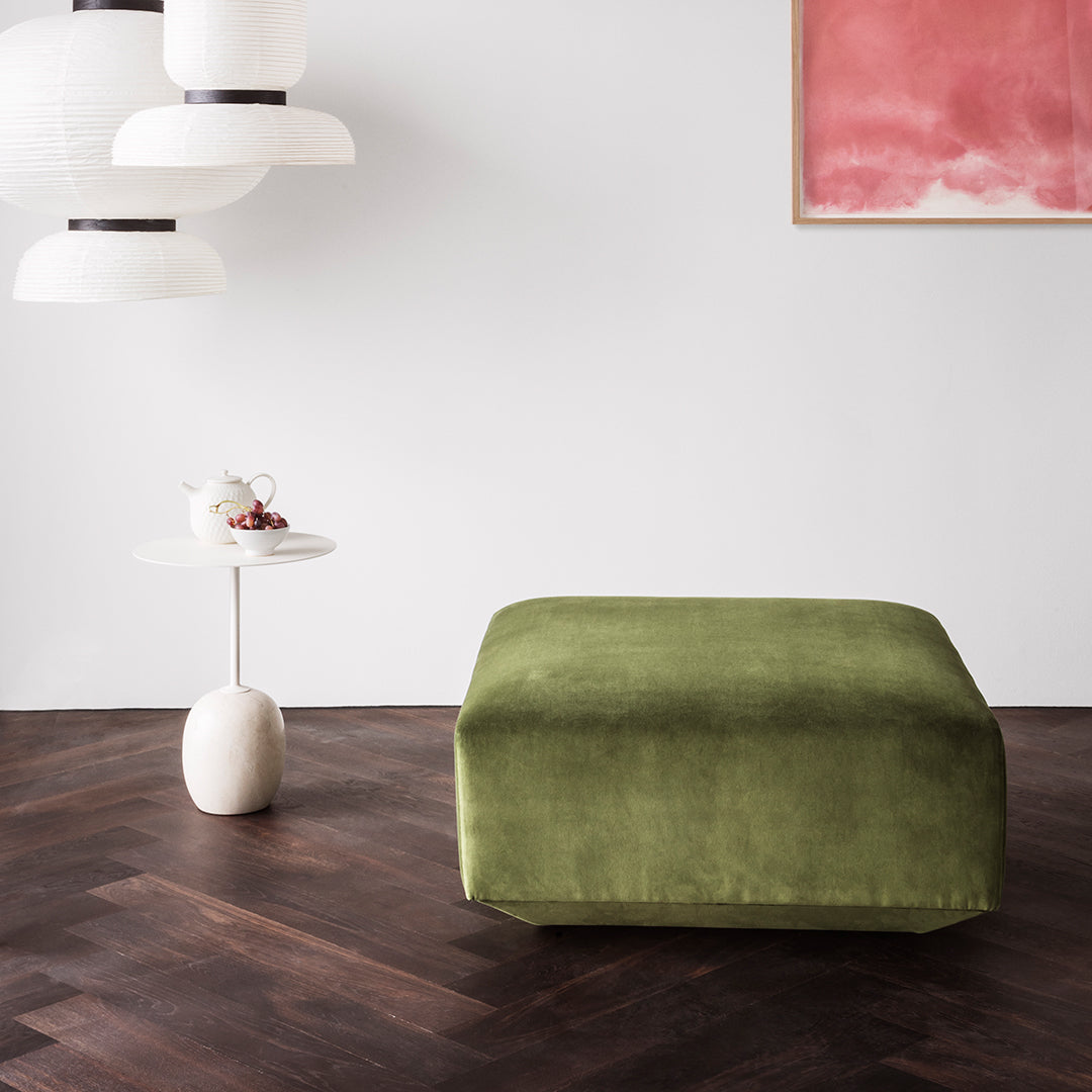 Green upholstered ottoman on a dark hardwood floor, complemented by minimalist decor and soft, neutral tones.