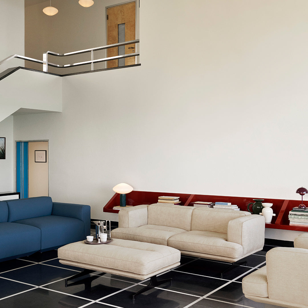 Modern living room with beige and blue sofas, red accents, and a black and white tiled floor. Clean, minimalist design.