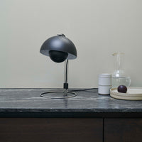 Black and chrome table lamp with a modern design, featuring a smooth, rounded shade and minimalistic base on a gray marble surface.