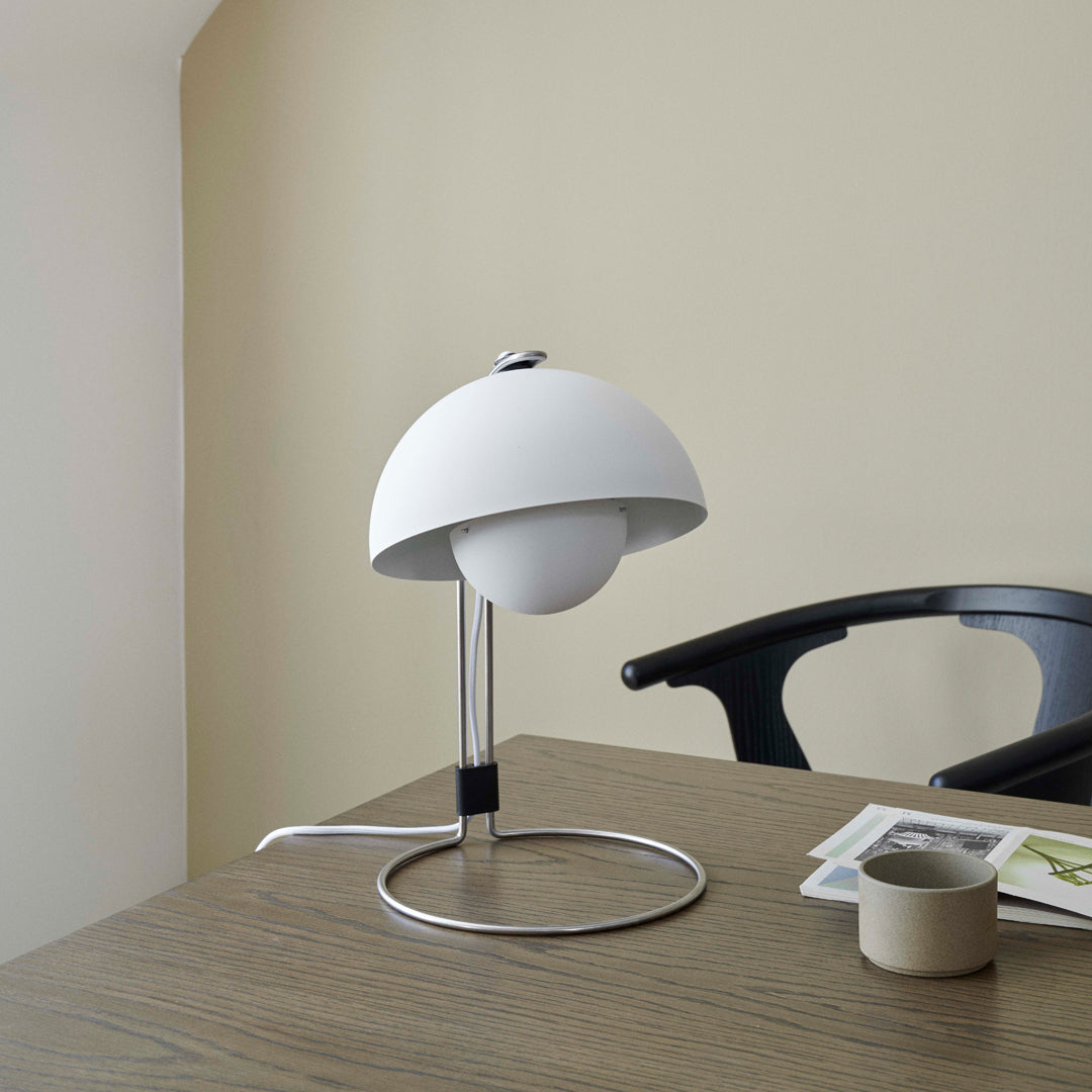 Modern white lamp with a rounded shade and sleek chrome base, set against a neutral beige backdrop.