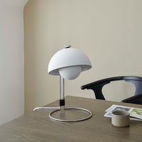 Modern white lamp with a rounded shade and sleek chrome base, set against a neutral beige backdrop.