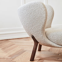 Textured cream fabric armchair with rounded back and dark wood legs, set against a light wooden floor.