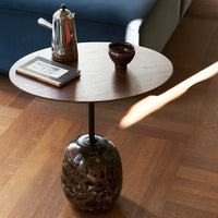 Round wooden tabletop with smooth brown finish, set on a polished marble base, on a warm wooden floor.