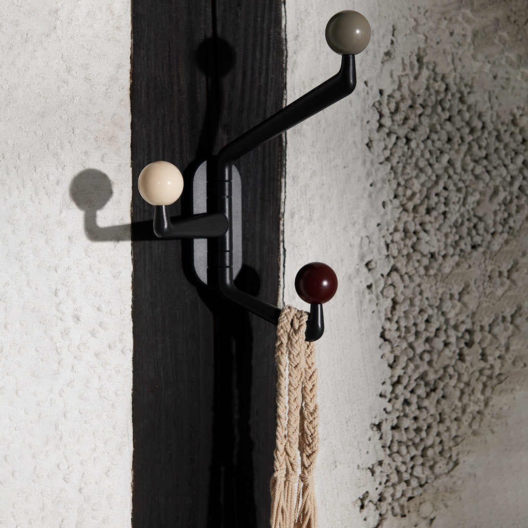 Black wall hook with cream, gray, and burgundy round knobs, set against a textured white background.