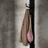 Brown coat hanging on a black wall hook, with a pink net bag, against a textured gray wall backdrop.