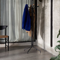 "Black metal coat rack with wood accents, featuring a solid blue jacket and beige coat against a textured concrete background."