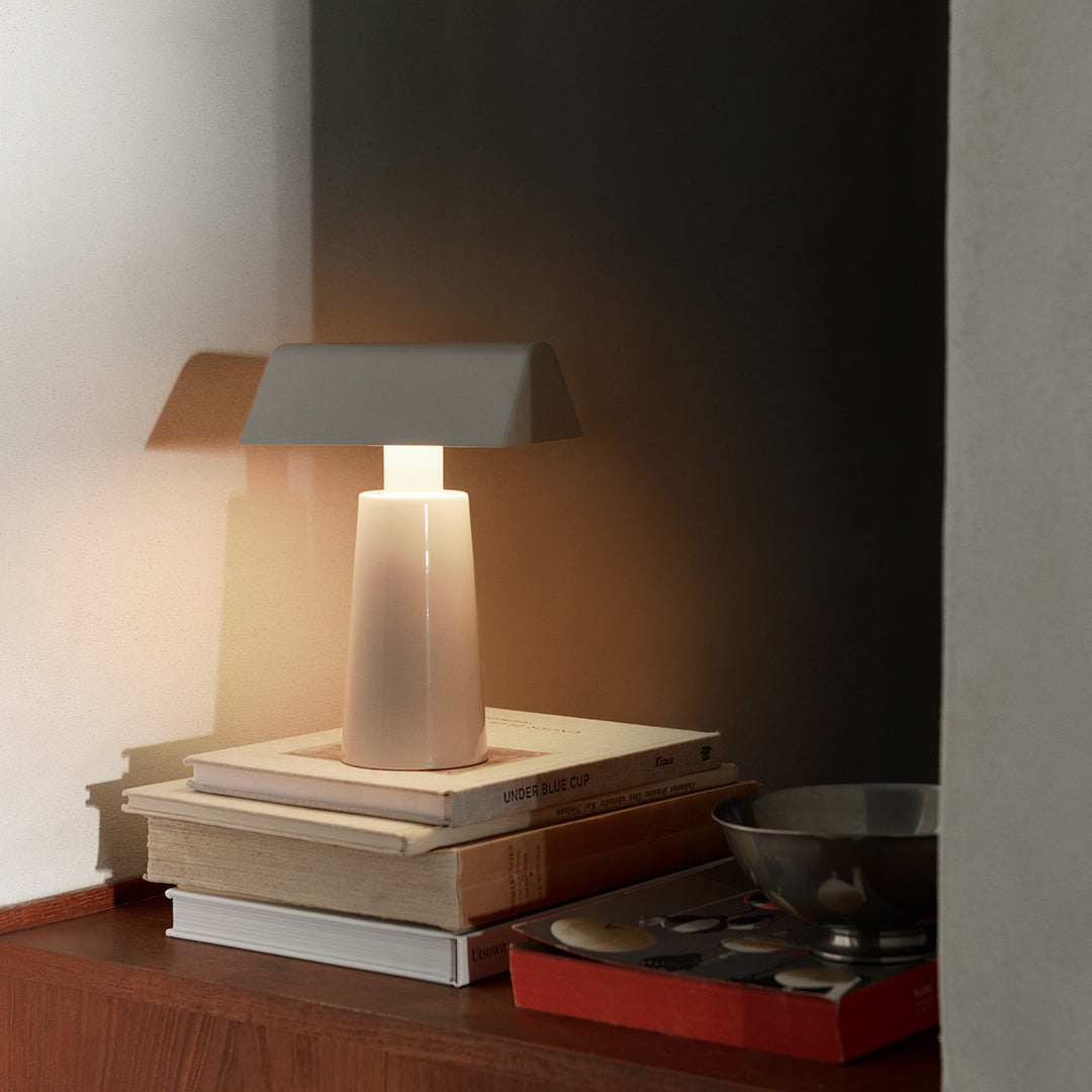 Modern lamp with a gray shade, white base, and soft warm light, styled on stacked books and minimalistic decor.