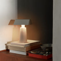 Modern lamp with a gray shade, white base, and soft warm light, styled on stacked books and minimalistic decor.