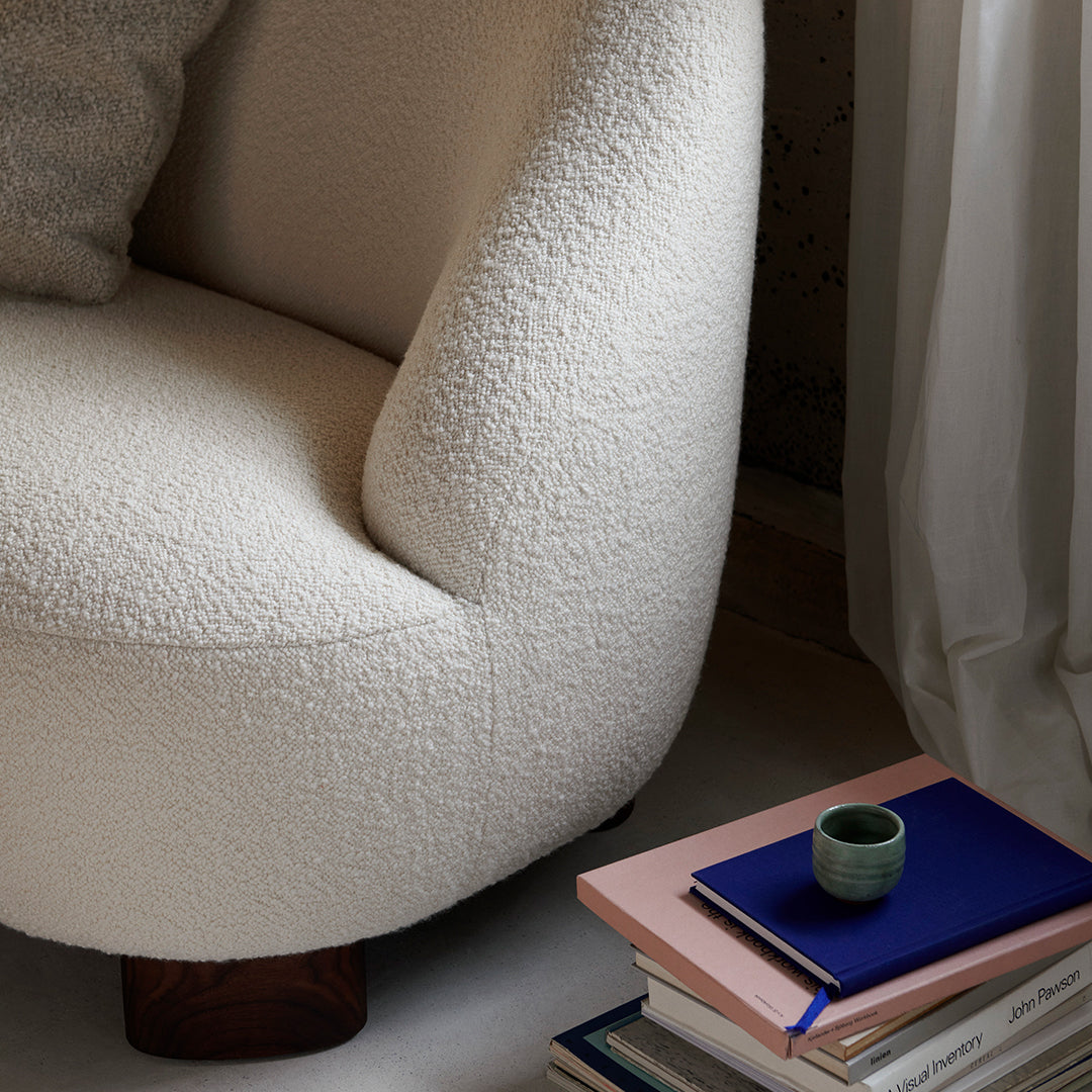 Cream textured chair with a rounded design, complemented by pastel-colored books and a small green cup.