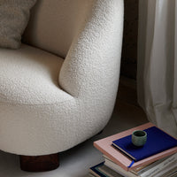 Cream textured chair with a rounded design, complemented by pastel-colored books and a small green cup.
