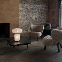 Modern lamp with an oval glass design, set against a textured brick wall and complemented by neutral-toned upholstered chairs.