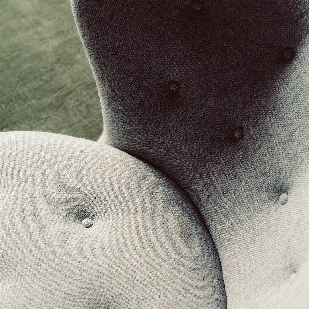 Gray upholstered chair close-up, showcasing soft fabric texture and button-tufted design against a green backdrop.