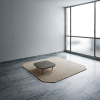 Beige octagonal rug with a grey square table on a polished marble floor, set against a minimalist backdrop.